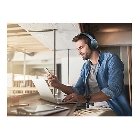 Mann mit KopfhÃ¶rern am Laptop, Smartphone in der Hand. Er sitzt in einem CafÃ©.