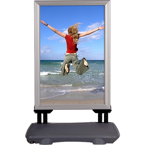 Advertising board showing a woman jumping on the beach. The board stands on a grey stand.