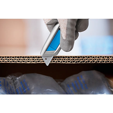 Une main gantée grise utilise un cutter bleu pour ouvrir une boîte en carton.