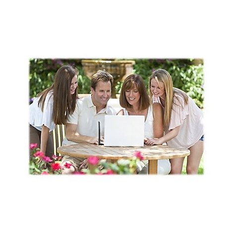 Eine Familie sitzt an einem Tisch im Freien und schaut auf einen Laptop-Bildschirm. Die Eltern und zwei Töchter wirken glücklich.