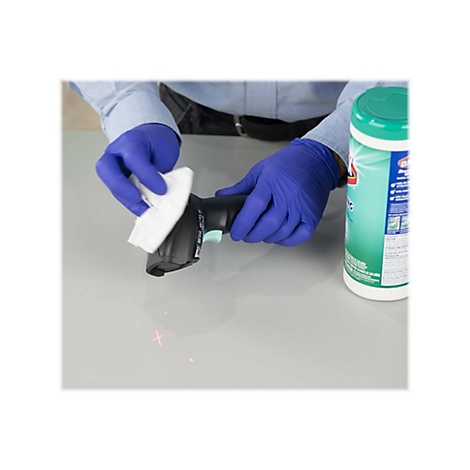 Person reinigt Barcode-Scanner mit einem Wischtuch, trÃ¤gt blaue Handschuhe, daneben DesinfektionstÃ¼cher.