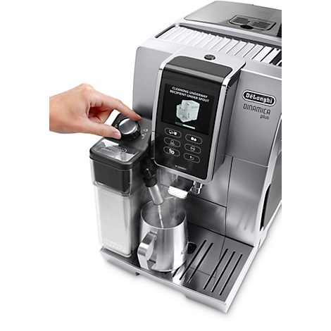 Eine Person bedient eine silberfarbene De'Longhi Dinamica Plus Kaffeemaschine. Auf dem Display wird die Reinigung angezeigt. Dampf kommt aus dem Ausguss.