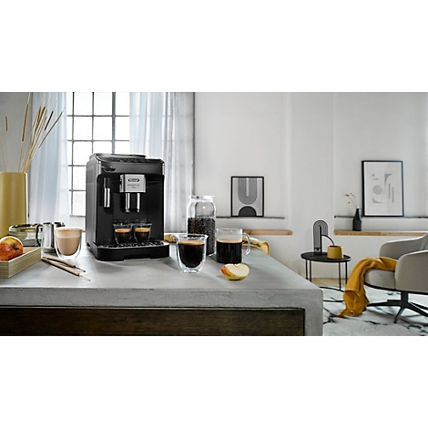 Schwarze Espressomaschine mit zwei Tassen Kaffee auf einem Tisch. Auf dem Tisch befinden sich auch Kaffeebohnen, Gläser und ein Apfel.