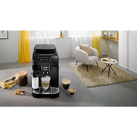 Schwarze Kaffeemaschine in einem Wohnzimmer, daneben eine Tasse Kaffee und ein gemütlicher Sessel. Helle Atmosphäre.