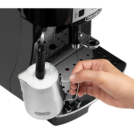 Nahaufnahme einer schwarzen Kaffeemaschine mit Milchschaum in einer Kanne. Eine Hand hält die Kanne.