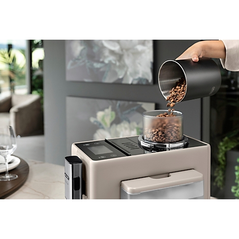 Kaffeebohnen werden in eine Kaffeemaschine gefüllt. Graue Kaffeemaschine auf einer hellen Arbeitsplatte.