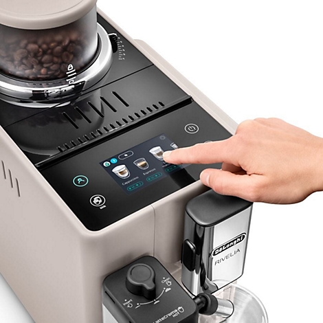 Nahaufnahme einer Kaffeemaschine. Ein Finger berührt den Bildschirm, auf dem Cappuccino, Espresso und weitere Kaffeespezialitäten ausgewählt werden können.