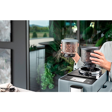 Une personne tient un récipient à grains de café. Un deuxième récipient est placé sur une machine à café.