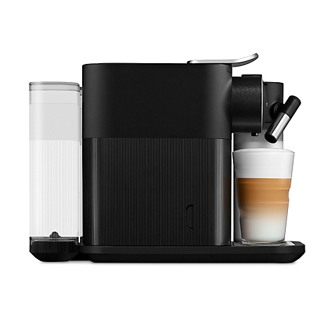 Schwarze Kaffeemaschine mit Milchkaffee in einem Glas. Rechts ein Auslauf, links ein Wassertank. Auf weißem Hintergrund.