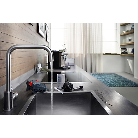 Roestvrijstalen kraan met stromend water in een keuken. Koffiemachine en raam op de achtergrond.