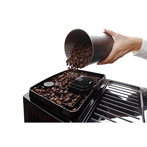 Een hand giet koffiebonen uit een zilveren container in een koffiemachine.