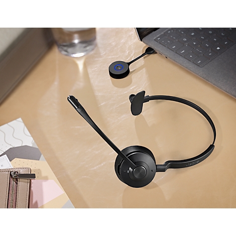 Black headset and accessories on a table. Laptop in the background.