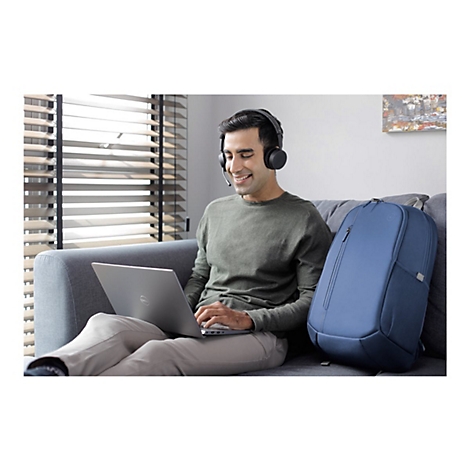 Ein Mann sitzt mit KopfhÃ¶rern und Laptop auf dem Sofa, lÃ¤chelnd. Blaue Tasche daneben.