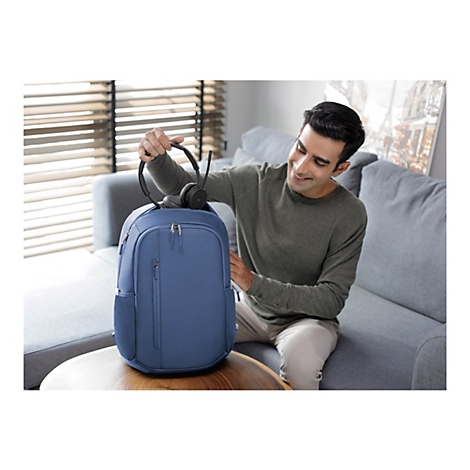 Ein lÃ¤chelnder Mann sitzt auf einem Sofa, hÃ¤lt KopfhÃ¶rer und verstaut sie in einem blauen Rucksack.