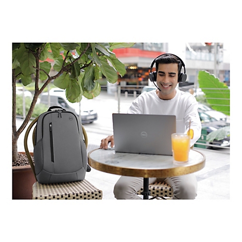 Mann arbeitet mit Laptop und KopfhÃ¶rern drauÃŸen. Ein grauer Rucksack steht daneben.