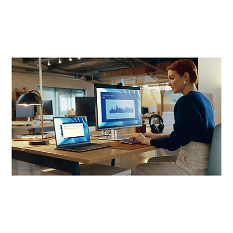 Eine Frau arbeitet an einem Schreibtisch mit Laptop und Monitor. Sie tippt auf der Tastatur. Auf dem Bildschirm Diagramme.