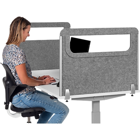 A woman is sitting at a desk with a partition typing on a keyboard. A laptop is partially visible.
