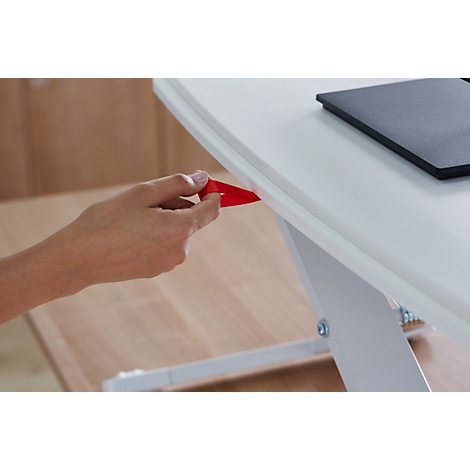 Hand pulling a red strap under a white desk. A black notebook lies on the right.