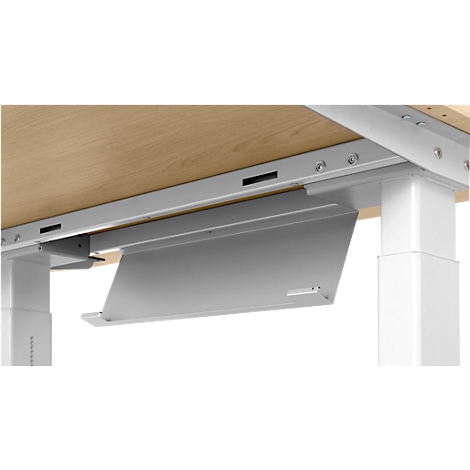 Close-up of the underside of a desk. A silver cable tray is mounted under the wooden top. The metal construction shows screws.