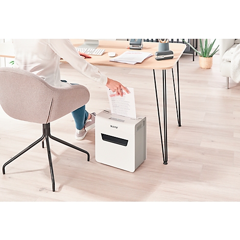 Personne jetant du papier dans une déchiqueteuse blanche. Bureau : clavier, porte-stylo, plante.