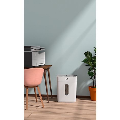 Bureau avec déchiqueteuse et imprimante. Une chaise est à gauche. Une plante en pot à droite.