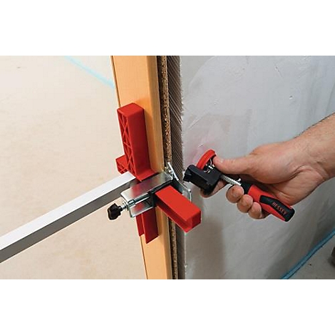 Hand houdt gereedschap vast om lijsten aan muur en deurkozijn te bevestigen. Rood en zwart gereedschap fixeert zilveren strip.