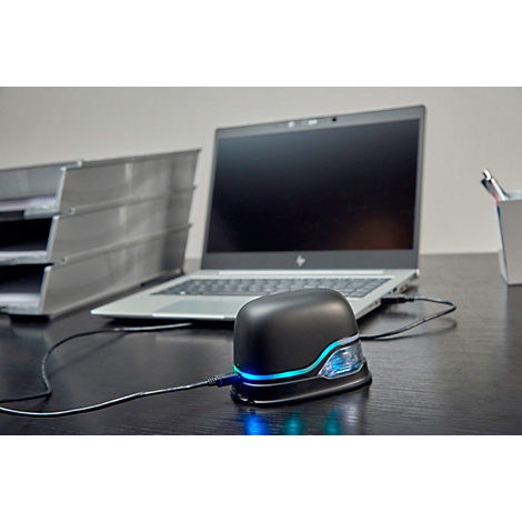 A black device with blue light connected to a laptop. In the background a filing tray and pens.