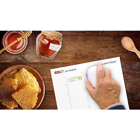 A table with honey, honeycomb, honey jars, wooden spoon and a hand operating a mouse on a label sheet.