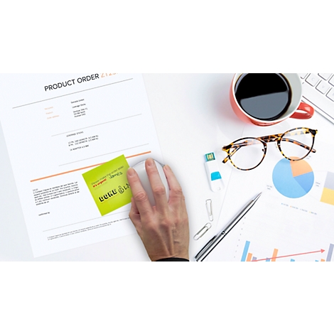 Close-up of a hand operating a mouse. Documents, a coffee cup, glasses, and charts are on the table.