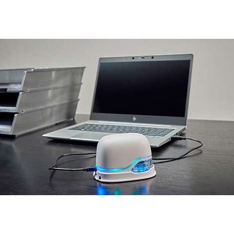 White device with blue lights, connected to a laptop. In the background, a stack of trays.