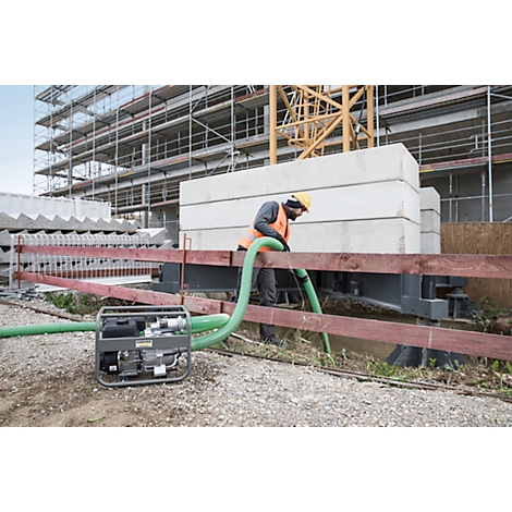 Construction worker in vest and helmet using a pump on a construction site. Crane and scaffolding in the background.