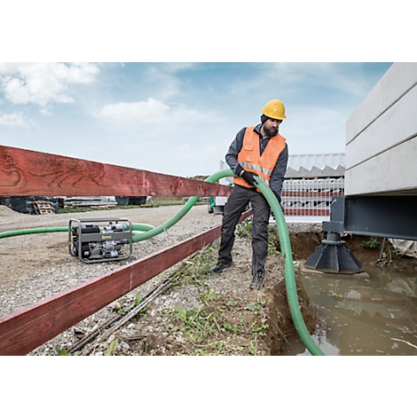 A construction worker in a safety vest and helmet holds a green hose, pumping water.