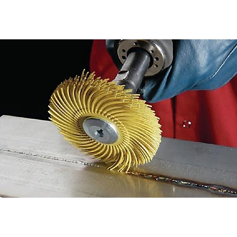 Brosse jaune nettoyant une soudure, bras ganté bleu tenant l'outil, chemise rouge en arrière-plan.