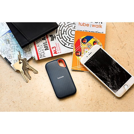 Smartphone avec écran fissuré, clés, portefeuille, guide de voyage et disque dur posés sur une table.