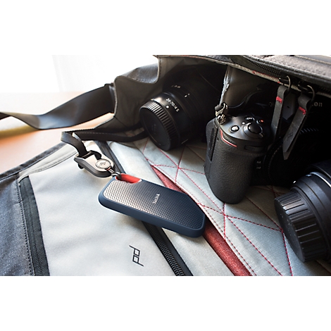 Disque dur bleu foncé avec un accent rouge sur un sac d'appareil photo. Plusieurs objectifs et un appareil photo en arrière-plan.