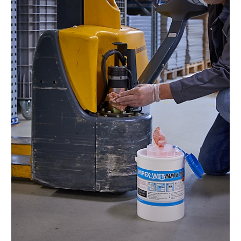 Un ouvrier nettoie un chariot élévateur avec une lingette. À côté se trouve un seau avec des lingettes de nettoyage.