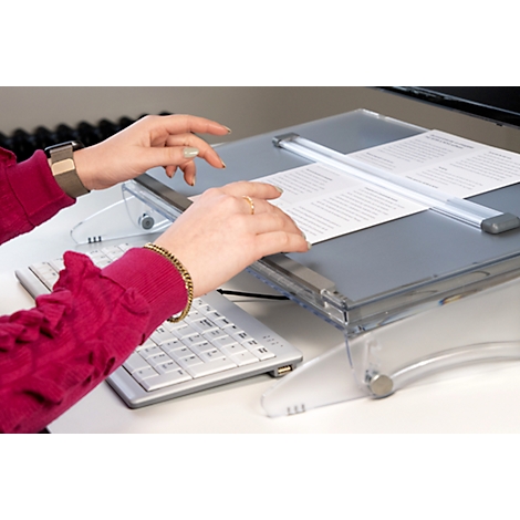Hands over keyboard and document holder. The woman wears gold jewelry and a smartwatch. A sheet of paper lies on the document holder.