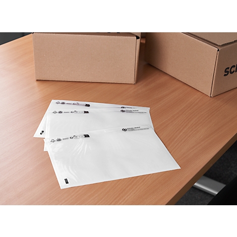 Three transparent envelopes lie on a wooden table. Cardboard boxes in the background.