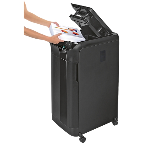 A person is placing paper into a black paper shredder. The lid is open.