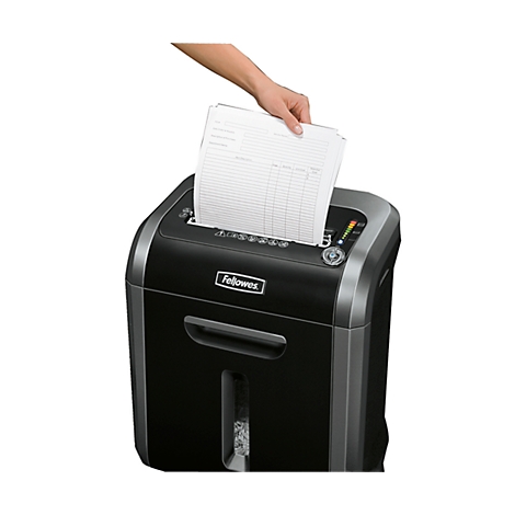 A hand inserts papers into a black shredder. The shredder has a control panel and the "Fellowes" logo.