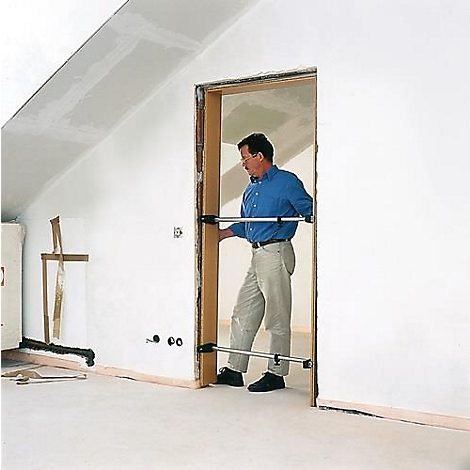 A man places a door frame with the help of two supports in an unfinished wall. Interior with sloping ceiling.