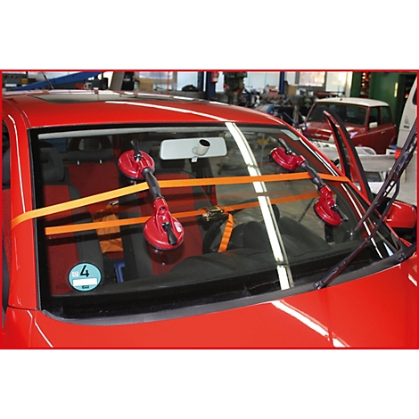 Rotes Auto mit Saugnäpfen und Gurten an der Windschutzscheibe, im Hintergrund eine Werkstatt.