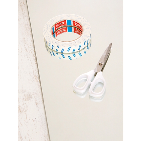 A roll of double-sided tape with red and blue markings and white scissors lie on a smooth surface.