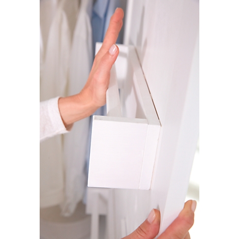 A hand touches a white detail of a wardrobe. The arm is wearing a white long-sleeved shirt.