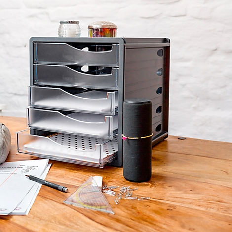 Grey drawer tower on a wooden board, open. Next to it, speaker and utensils, glasses on top.