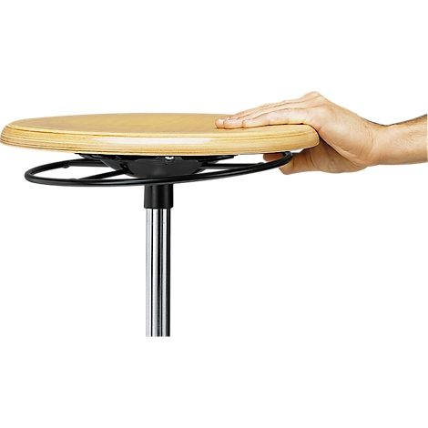 Der runde, helle Holz-Sitz eines Stehhockers, gehalten von einer Hand, die auf dem Sitz liegt.