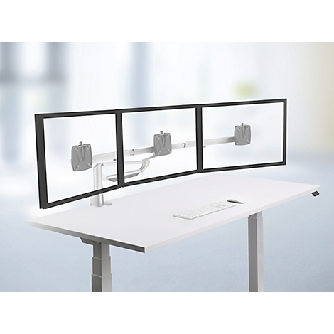 Drievoudige monitorstandaard op een witte bureau. Monitoren met dunne zwarte randen, metalen beugel. Bureau met toetsenbord, wazige achtergrond.