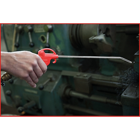 Eine Hand hält eine rote Druckluftpistole, die auf eine Maschine gerichtet ist. Metallspäne liegen daneben.