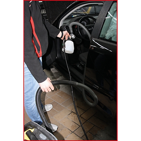 Ein Mann reinigt den Innenraum eines schwarzen Autos. Er hält einen Schlauch und eine Sprühflasche.