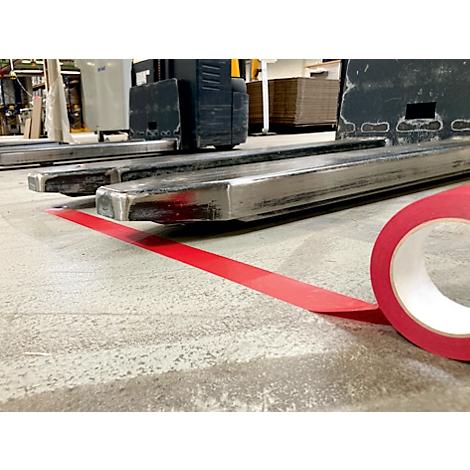 Red tape on concrete floor, forklift in the background.